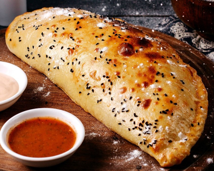 Darin's tasty Calzone topped with black sesame seeds and two small dipping sauces.